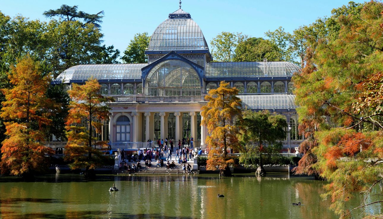 Scenic view of Palacio de Cristal surrounded by vibrant autumn trees at Retiro Park, Madrid.